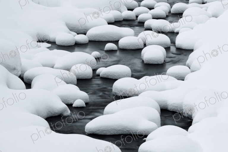 Close up of riverbed with snow-covered rocks in winter.