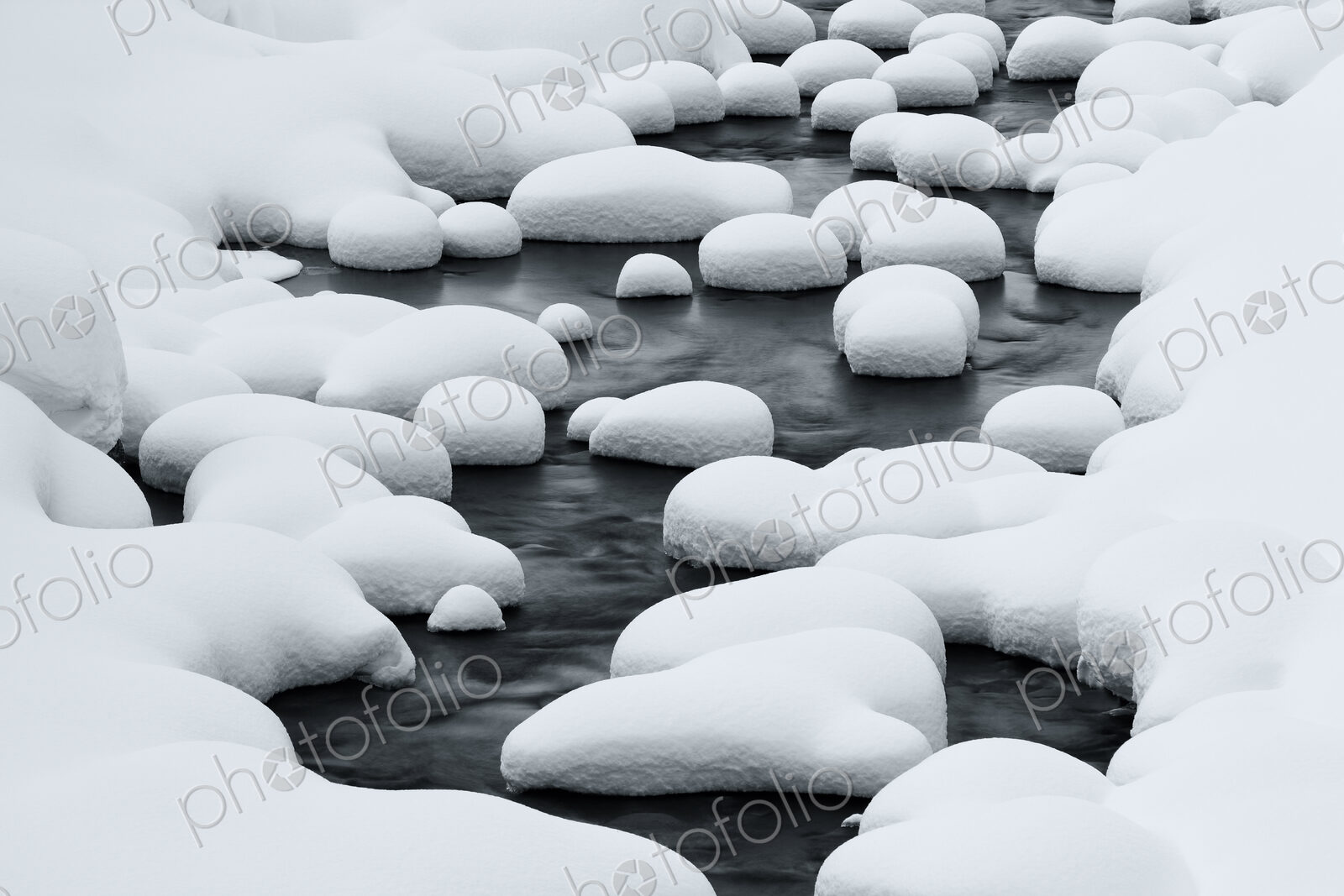 Close up of riverbed with snow-covered rocks in winter.