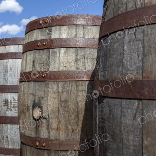Close-up of rustic wooden barrels with metal bands under a bright blue sky in Hill…