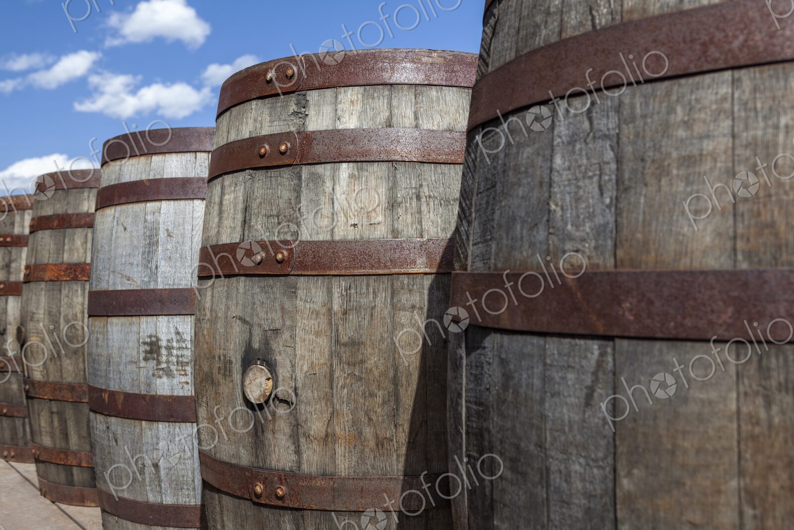 Close-up of rustic wooden barrels with metal bands under a bright blue sky in Hill…