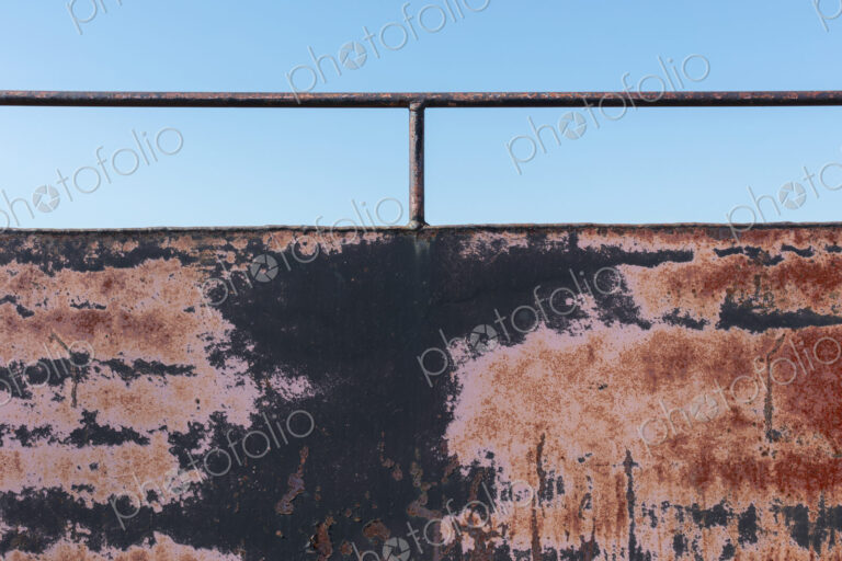 Close up of rusty black wall with railing.