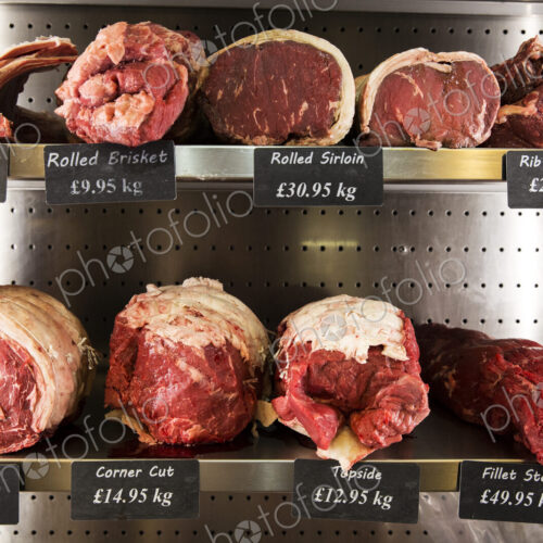 Close up of selection of cuts of lamb and beef on metal shelves in butcher shop.