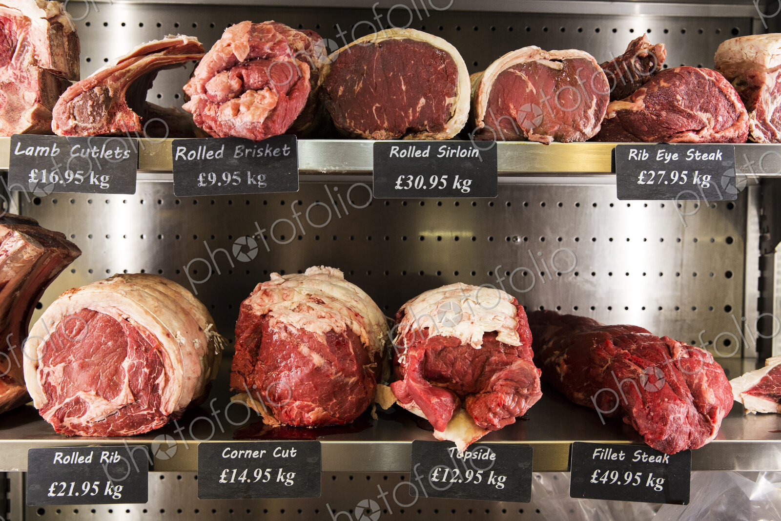 Close up of selection of cuts of lamb and beef on metal shelves in butcher shop.