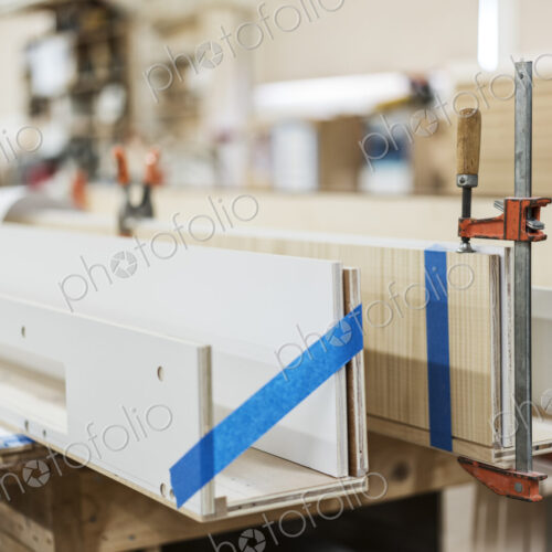 Close up of small bar clamps being used in a woodworking factory. Close up of small bar clamps being used in a woodworking factory.