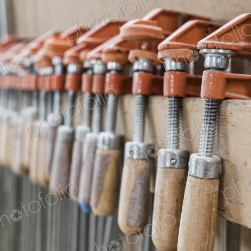 Close up of small bar clamps being used in a woodworking factory. Close up of small bar clamps being used in a woodworking factory.
