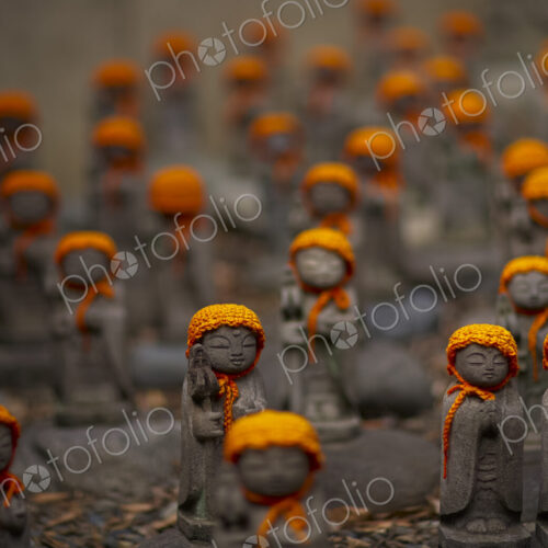 Close up of small brown Buddhist Jizo, Japanese stone statues, wearing orange hats, at…