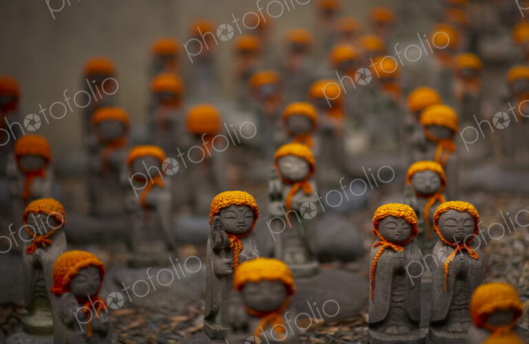 Close up of small brown Buddhist Jizo, Japanese stone statues, wearing orange hats, at…