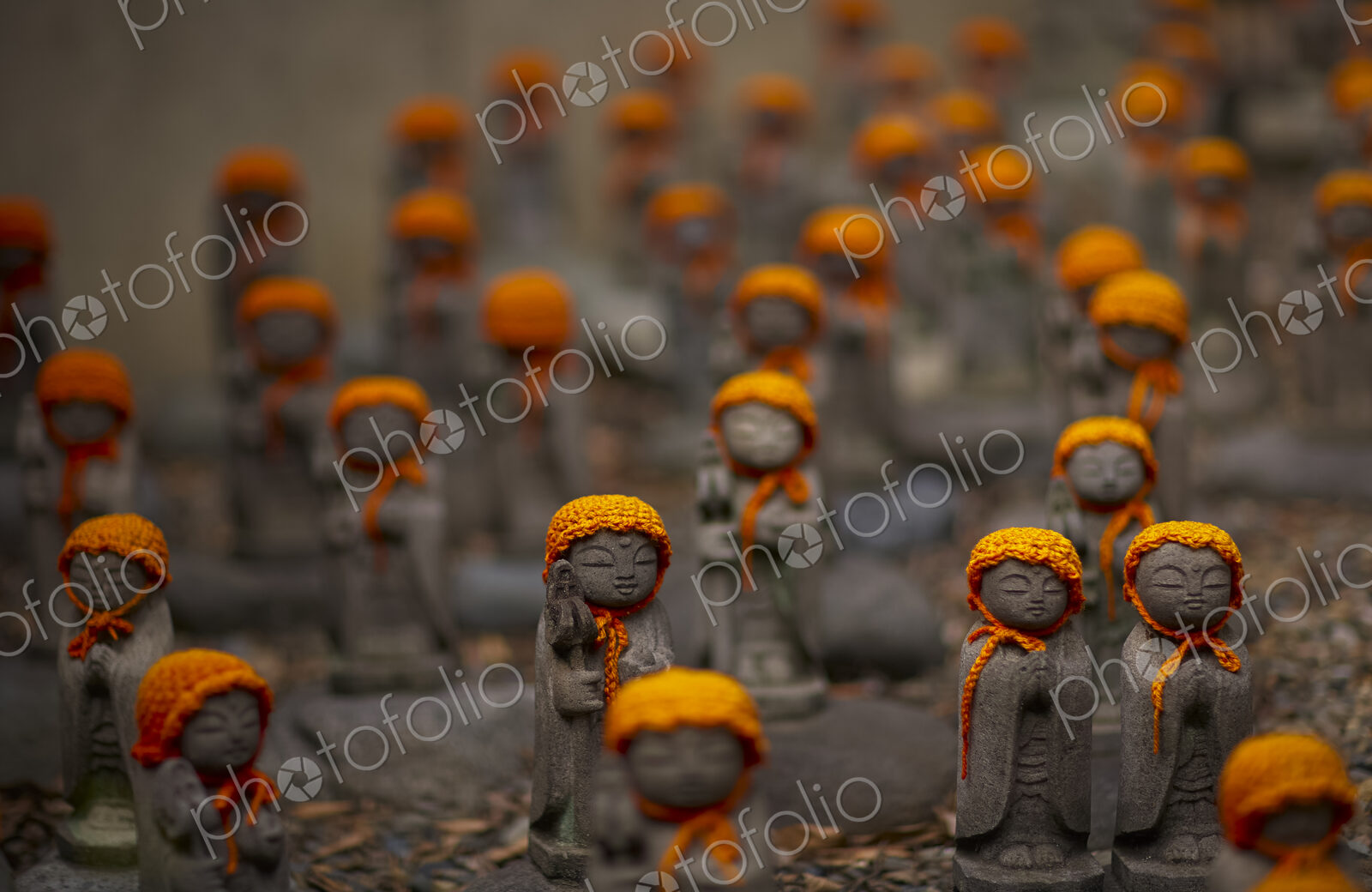 Close up of small brown Buddhist Jizo, Japanese stone statues, wearing orange hats, at…