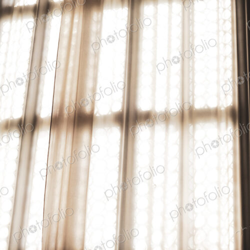 Close up of sunlight filtering through a net curtain in front of leaded glass window.
