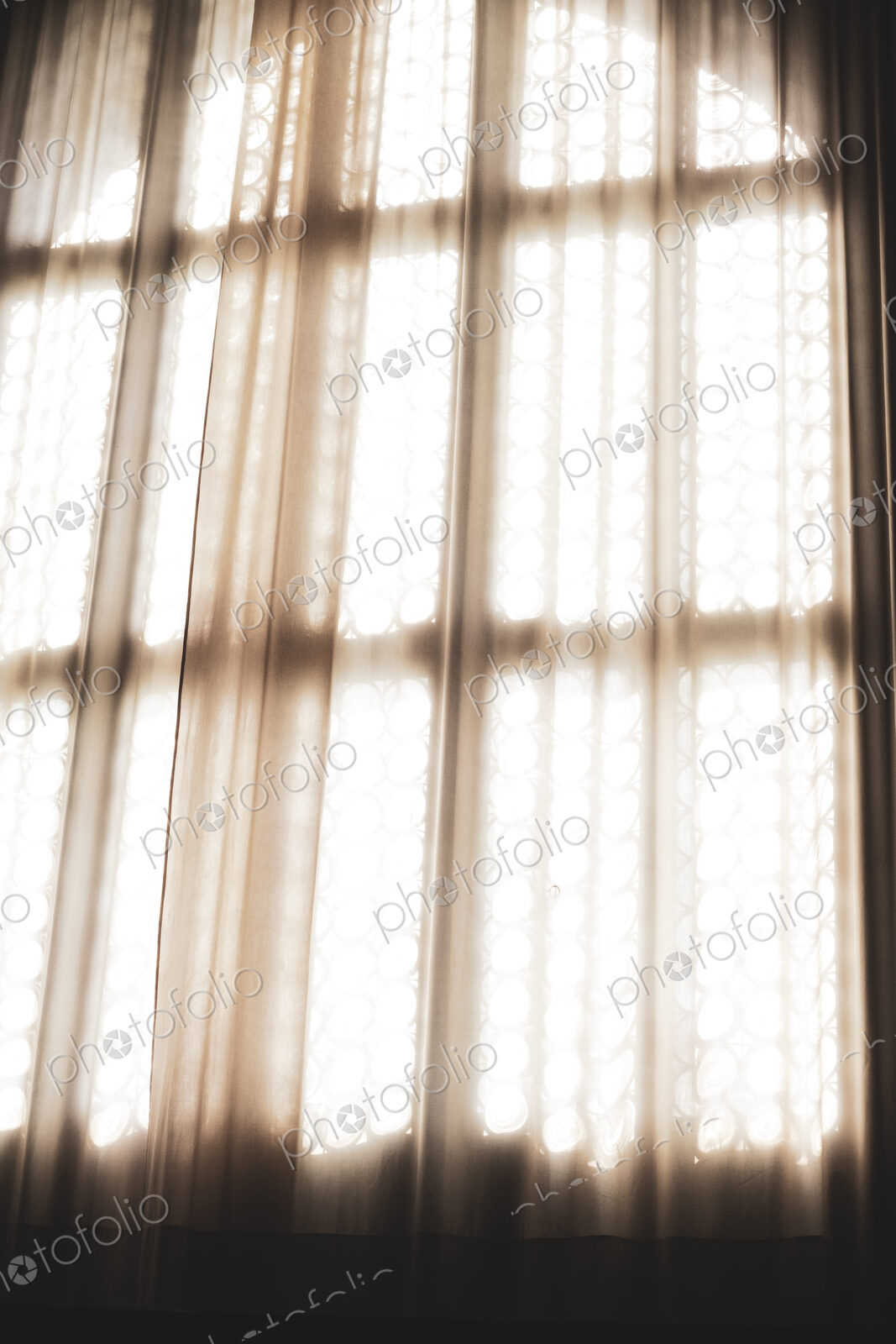 Close up of sunlight filtering through a net curtain in front of leaded glass window.