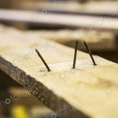 Close up of three rusty nails sticking out of a wooden plank.