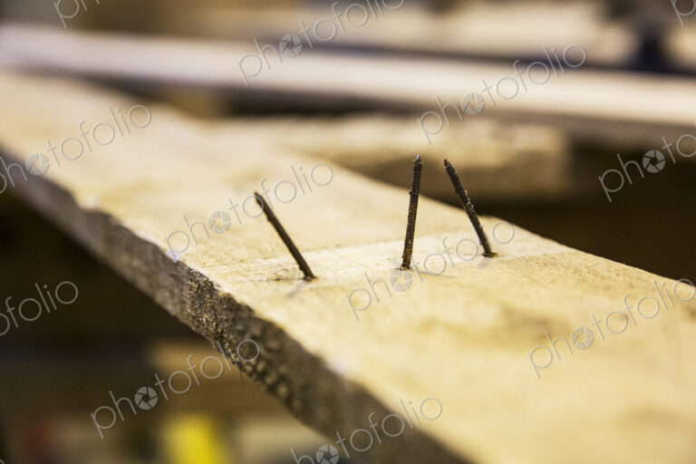Close up of three rusty nails sticking out of a wooden plank.