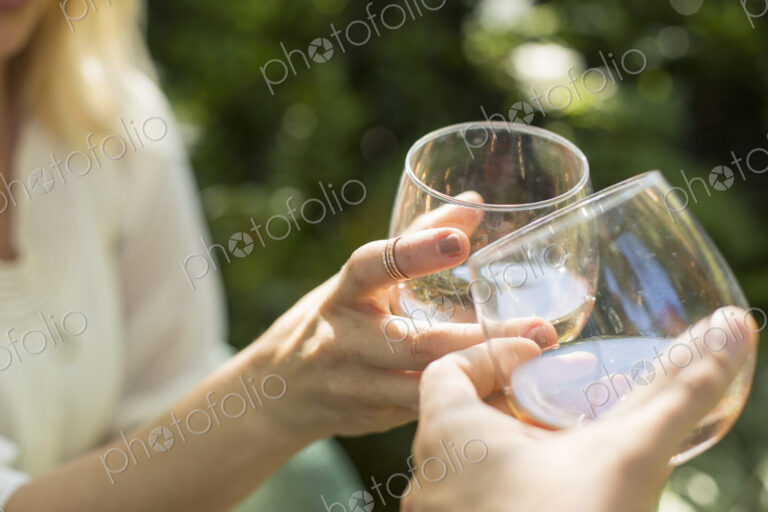 Close up of two people holding glasses with rose wine, toasting each other. Celebration.