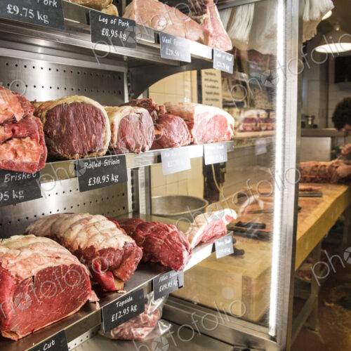 Close up of various cuts of beef on shelves in a butcher shop, man wearing apron… Close up of various cuts of beef on shelves in a butcher shop, man wearing apron…