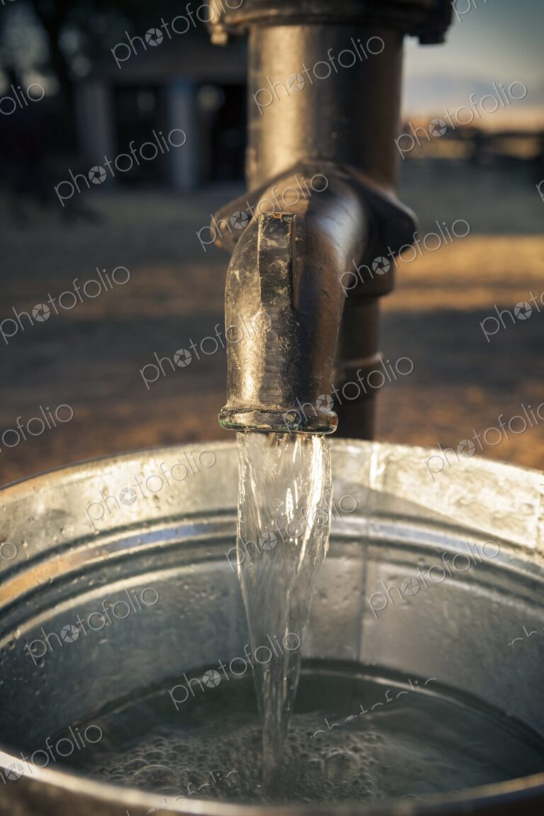 Close-up of water flowing from an old metal pump into a galvanized steel bucket. Rural…