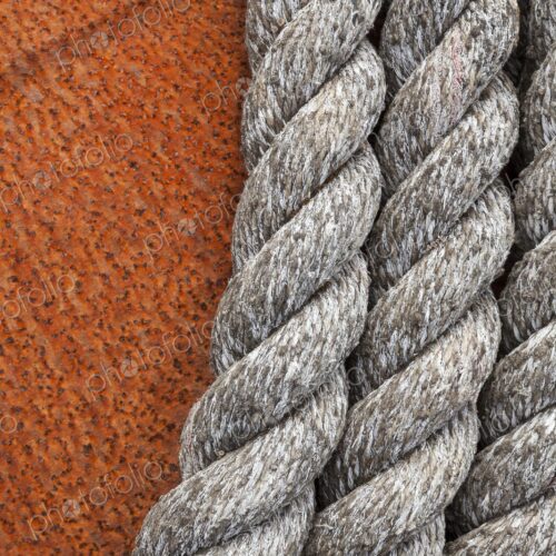 Close-up of weathered nautical rope coiled against the textured surface of a rusted… Close-up of weathered nautical rope coiled against the textured surface of a rusted…