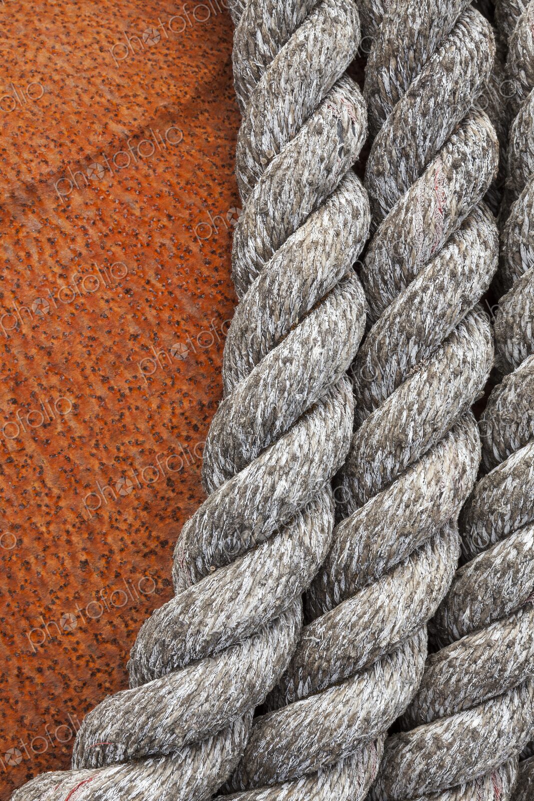 Close-up of weathered nautical rope coiled against the textured surface of a rusted…