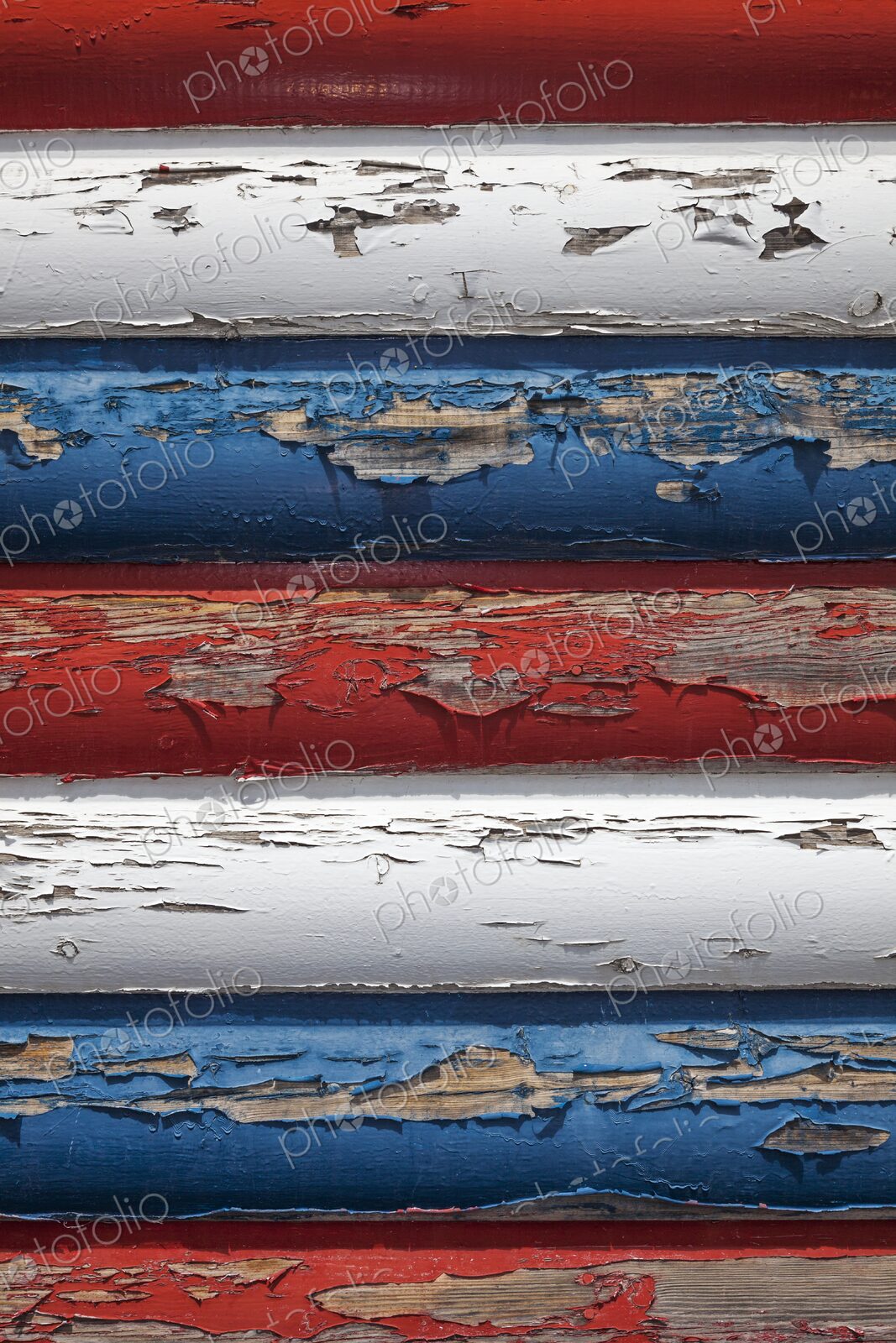Close-up of weathered red, white, and blue paint peeling off wooden boards, evoking…
