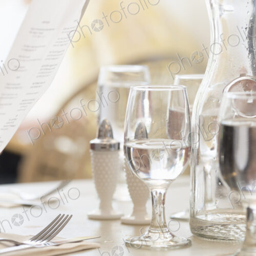 Close up of wine and water glasses and place settings at a table in a restaurant. A…