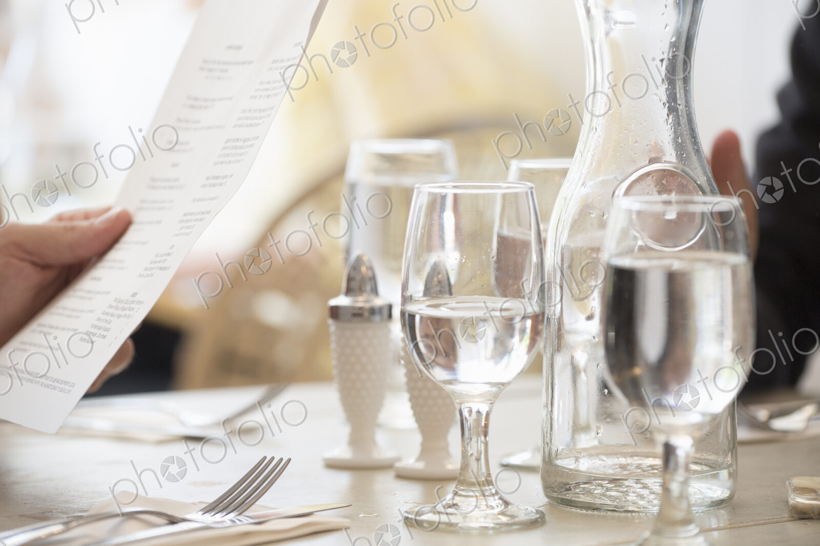 Close up of wine and water glasses and place settings at a table in a restaurant. A…