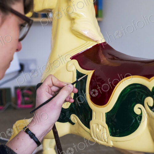 Close up of woman in workshop, painting traditional wooden carousel horse from…