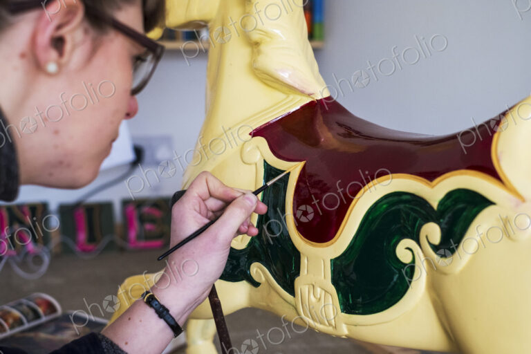 Close up of woman in workshop, painting traditional wooden carousel horse from…