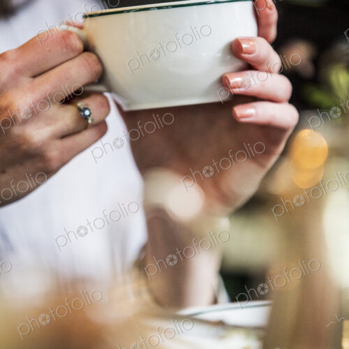 Close up of woman sitting at a table, holding white porcelain tea cup. Close up of woman sitting at a table, holding white porcelain tea cup.