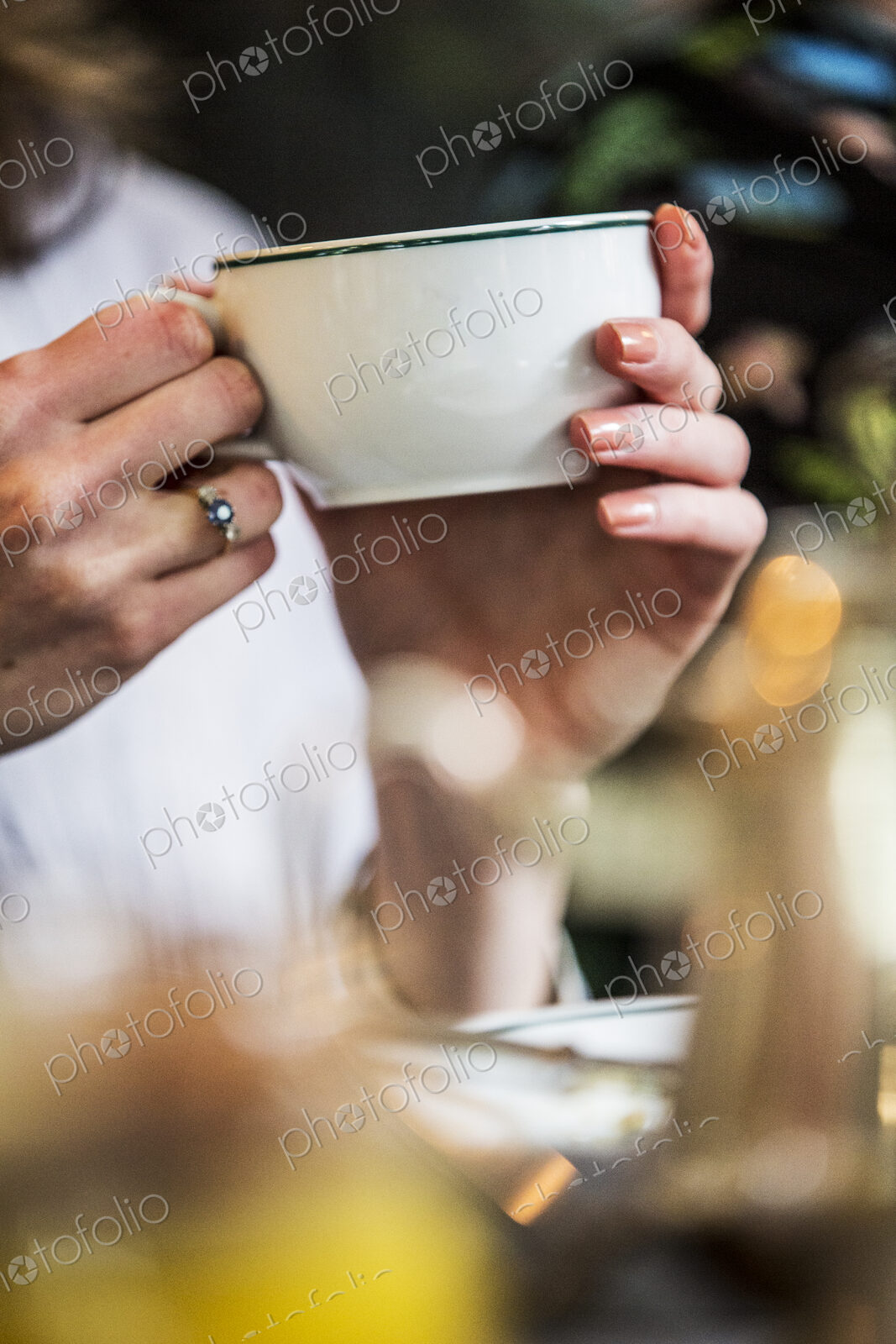 Close up of woman sitting at a table, holding white porcelain tea cup.
