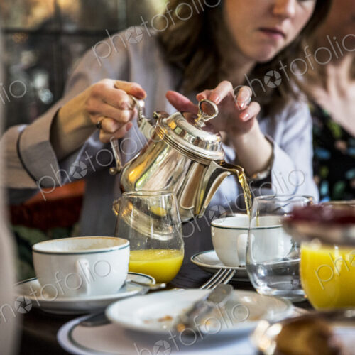 Close up of woman sitting at a table, pouring tea from silver tea pot. Close up of woman sitting at a table, pouring tea from silver tea pot.