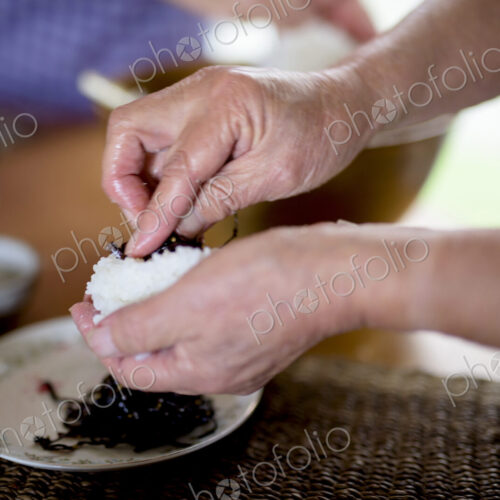 Close up of woman standing at a table in a kitchen, making sushi.