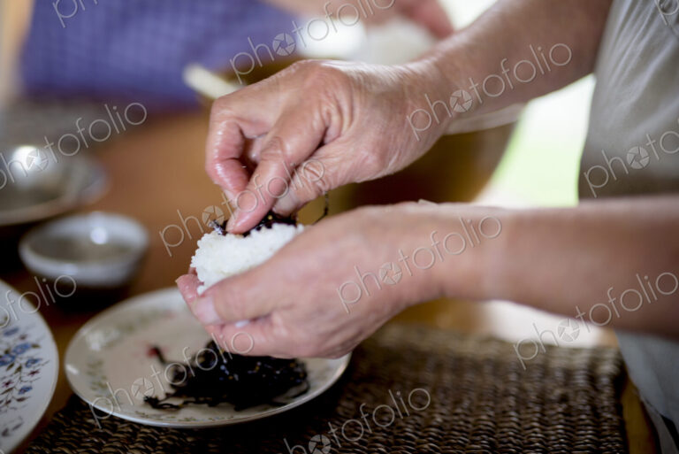 Close up of woman standing at a table in a kitchen, making sushi.