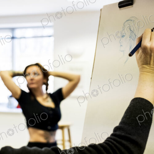Close up of woman standing at easel at a life drawing class drawing a model