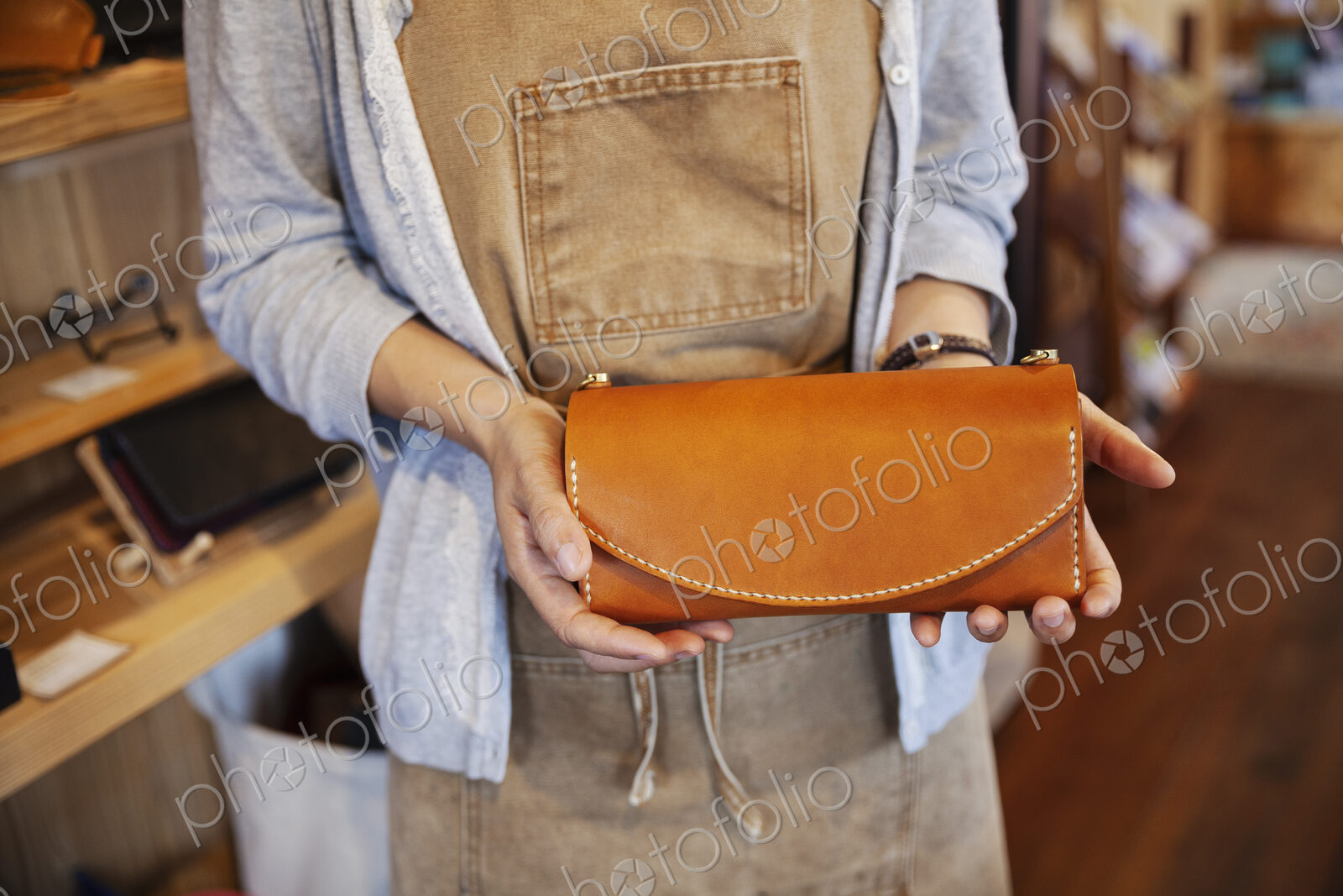 Close up of woman standing in a leather shop, holding tan leather clutch bag.
