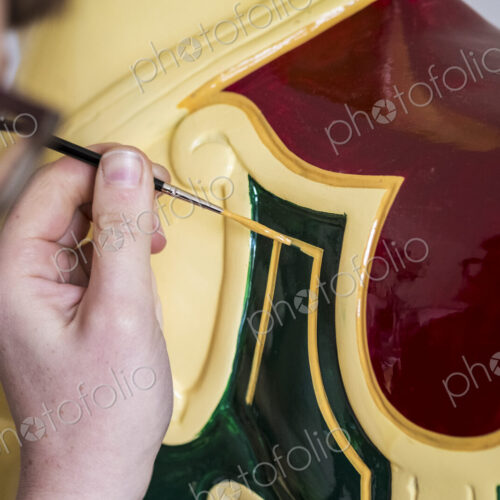 Close up of woman wearing glasses in a workshop, painting traditional wooden horse…