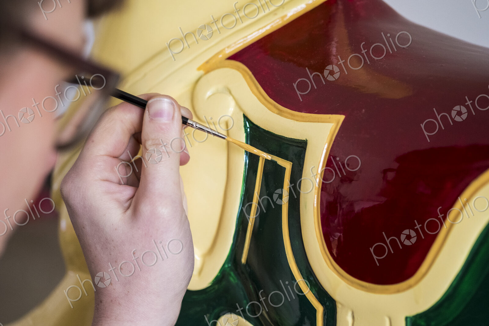 Close up of woman wearing glasses in a workshop, painting traditional wooden horse…