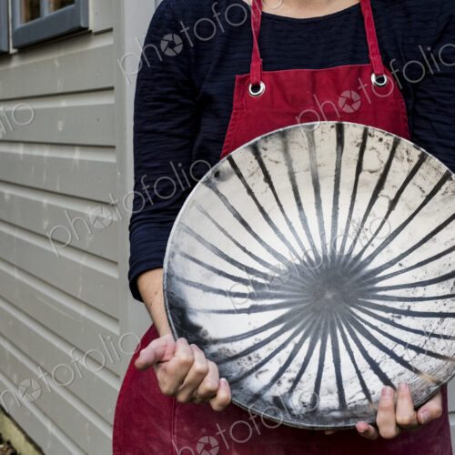 Close up of woman wearing red apron holding ceramic bowl with black line pattern.