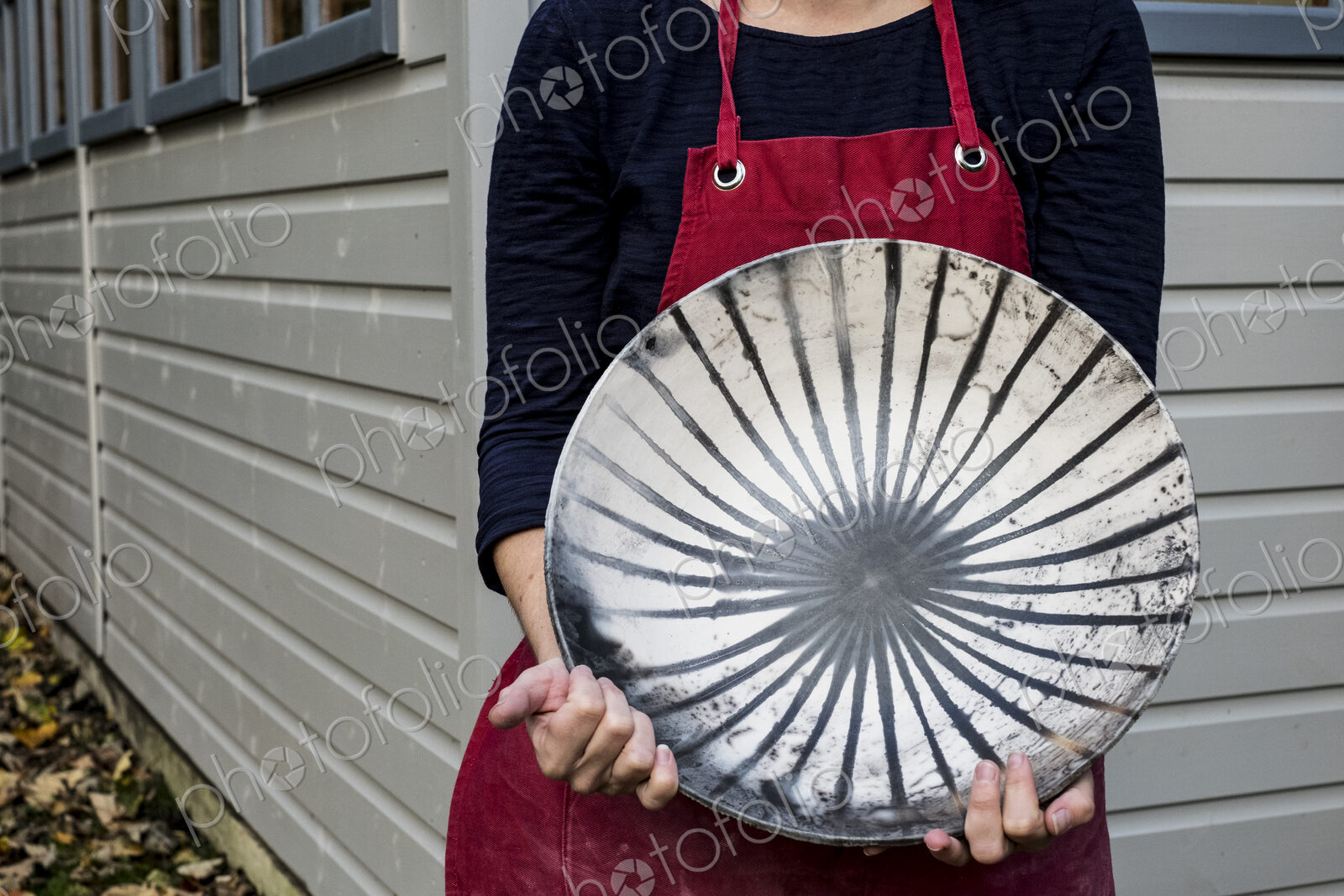 Close up of woman wearing red apron holding ceramic bowl with black line pattern.