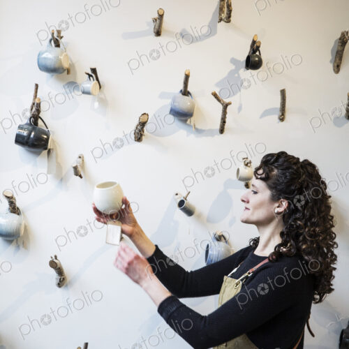Close up of woman with curly brown hair wearing apron standing in pottery shop,… Close up of woman with curly brown hair wearing apron standing in pottery shop,…
