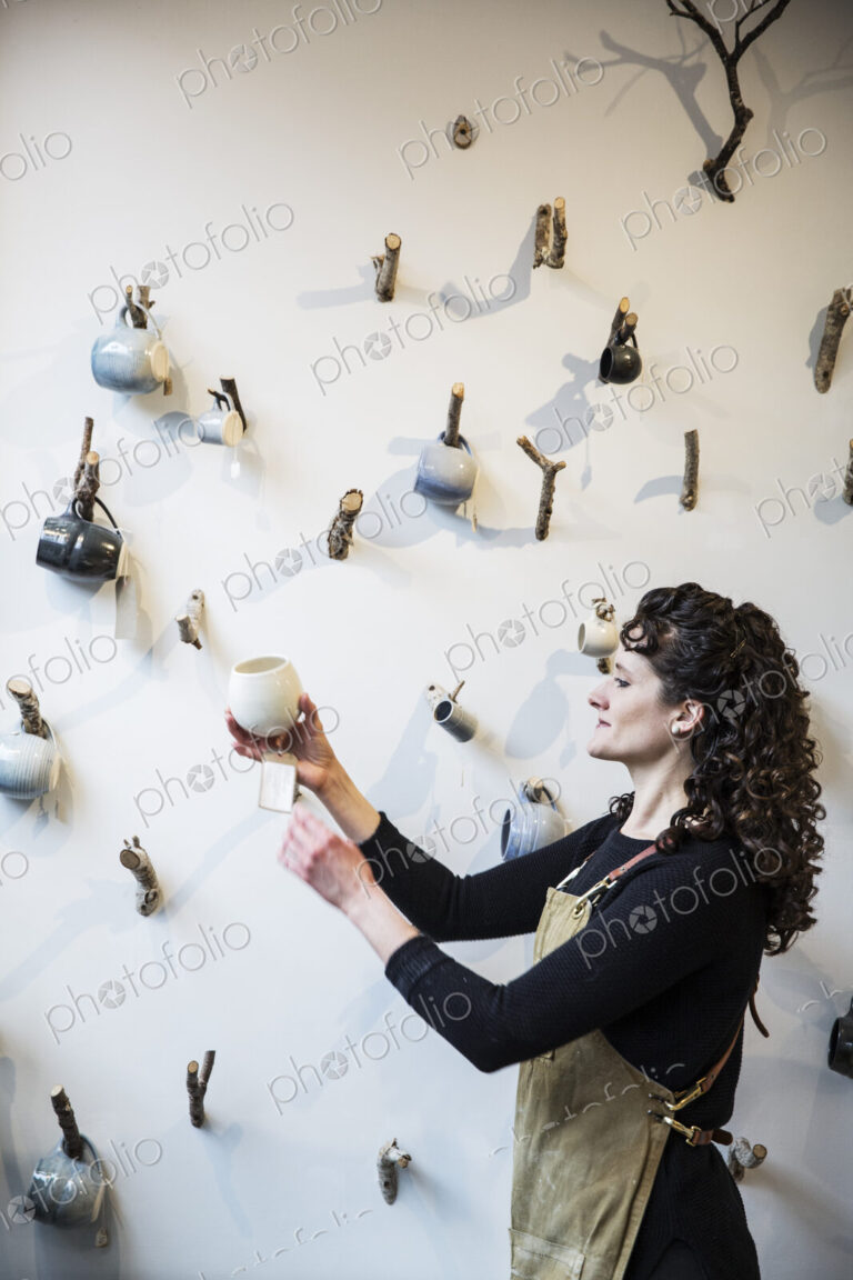 Close up of woman with curly brown hair wearing apron standing in pottery shop,…