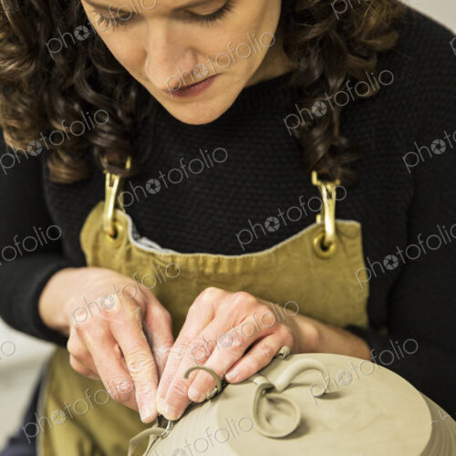 Close up of woman with curly brown hair wearing apron working on spherical clay vase… Close up of woman with curly brown hair wearing apron working on spherical clay vase…