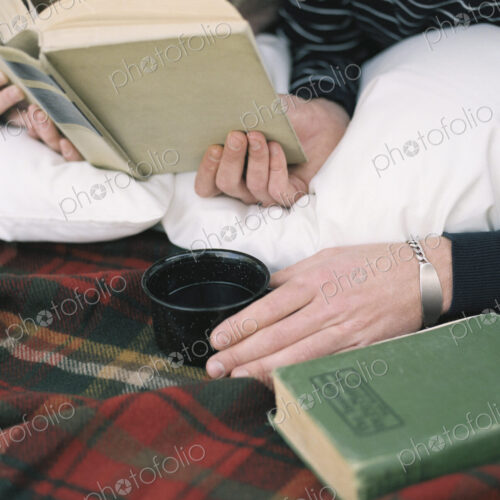 Close up of young man reading a book, holding a mug.