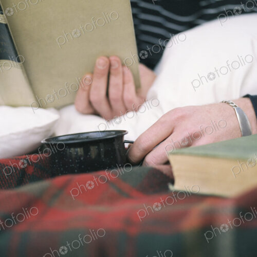 Close up of young man reading a book, holding a mug.
