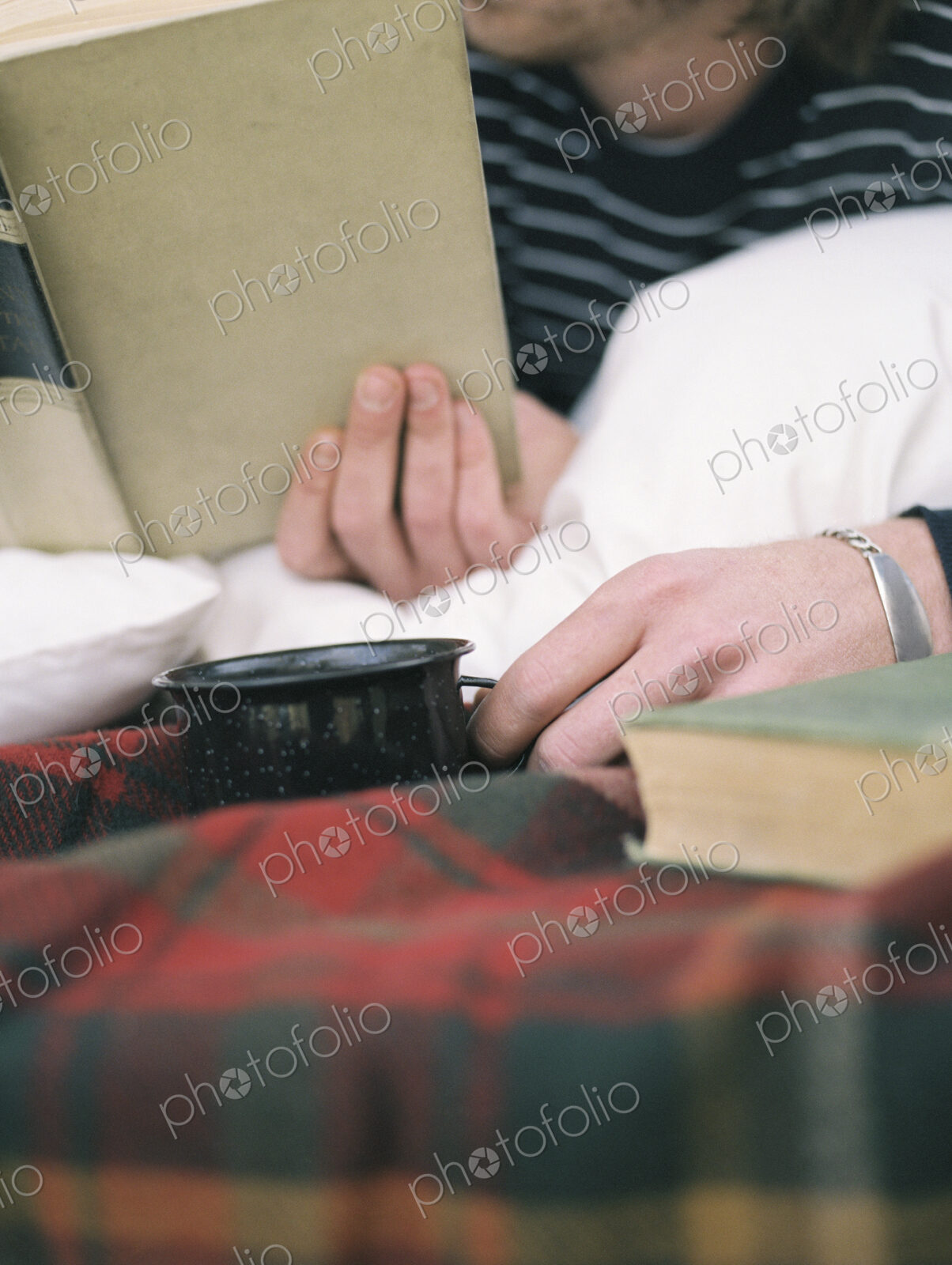 Close up of young man reading a book, holding a mug.