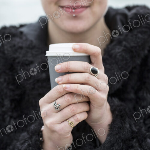 Close up of young woman wearing black furry jacket holding paper cup with hot drink. Close up of young woman wearing black furry jacket holding paper cup with hot drink.