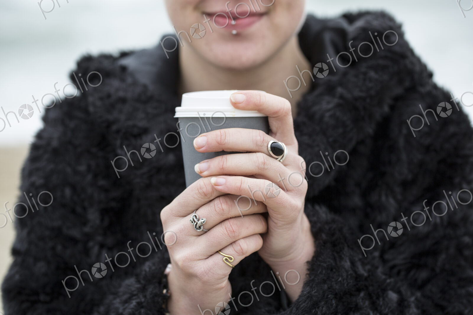 Close up of young woman wearing black furry jacket holding paper cup with hot drink.