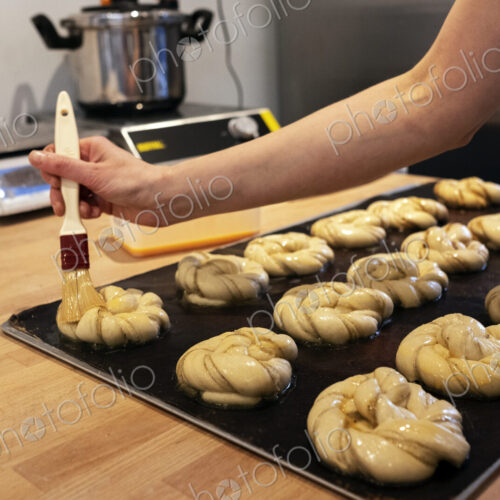 Close up person brushing cinnamon buns on a baking tray in an artisan bakery.