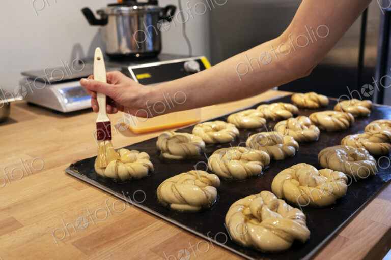Close up person brushing cinnamon buns on a baking tray in an artisan bakery.