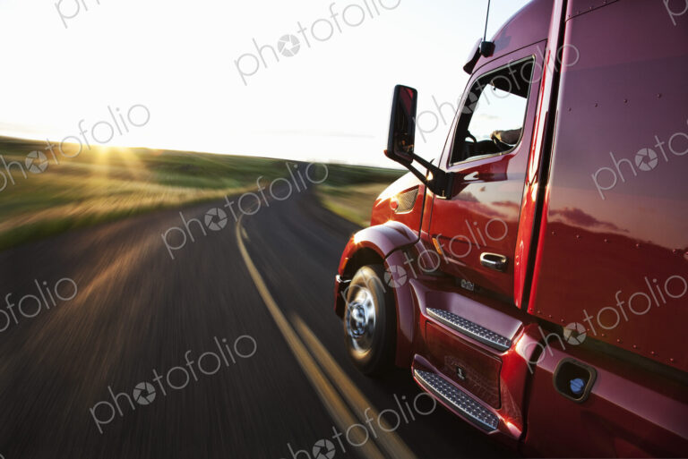 Close up side view looking forward of a commercial truck on a highway at sunset.