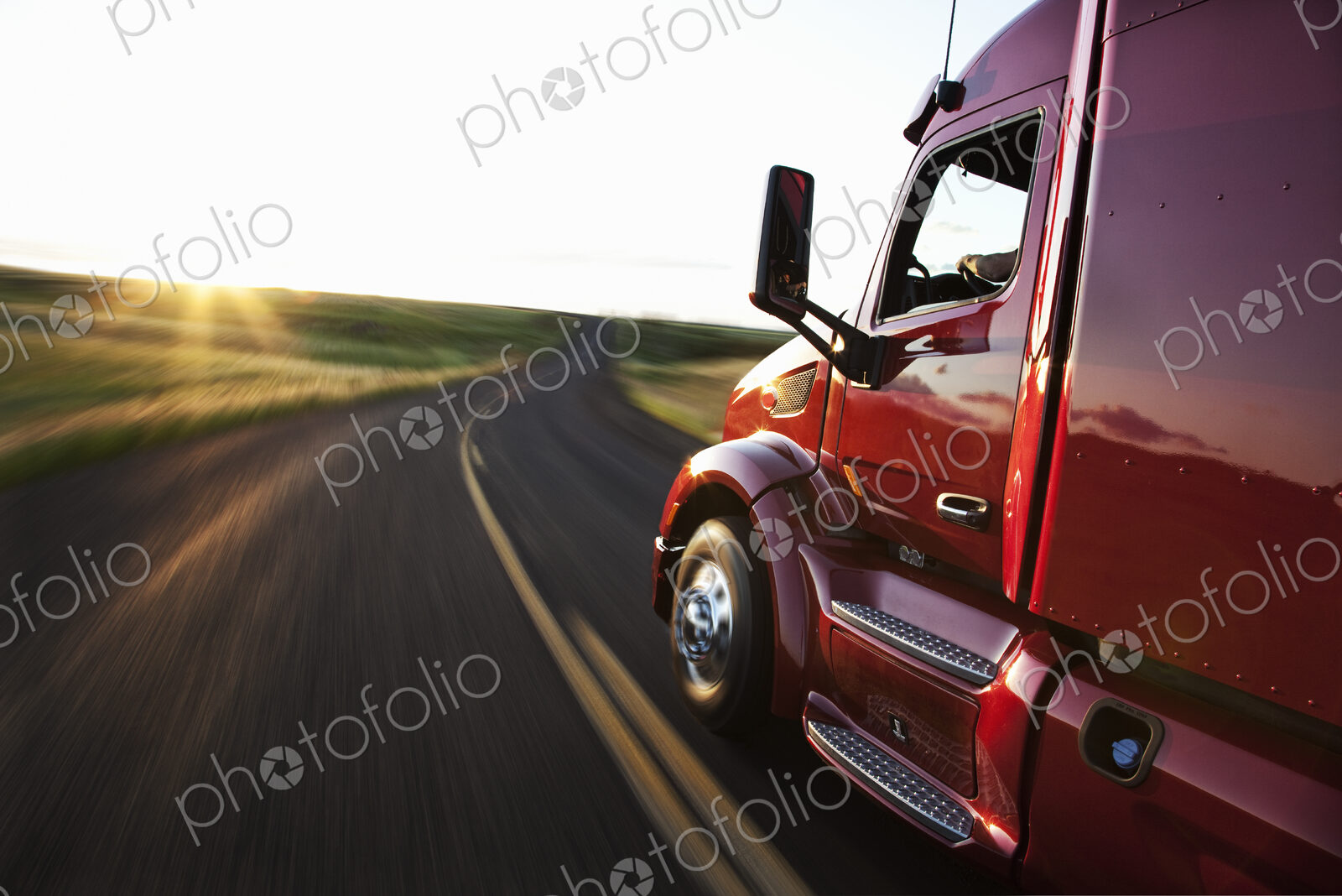 Close up side view looking forward of a commercial truck on a highway at sunset.