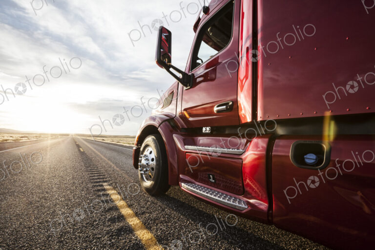 Close up side view looking forward of a commercial truck on a highway at sunset.